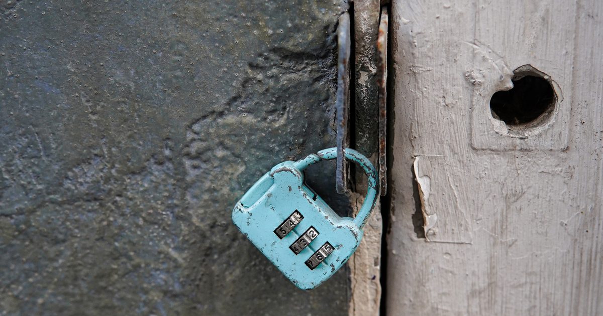 A worn turquoise combination padlock hanging from a rusty latch on a weathered door with peeling paint