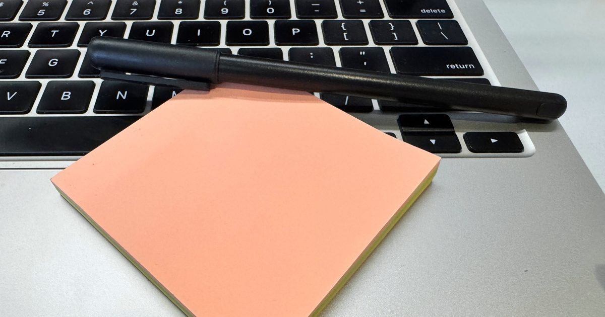 A peach sticky note pad and a black pen resting on a silver laptop keyboard, ready for jotting down ideas