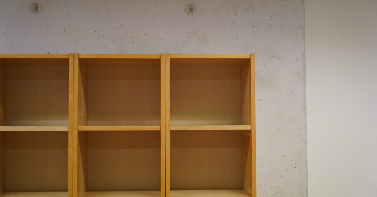An empty light wooden bookshelf with bare shelves standing against a grey concrete wall