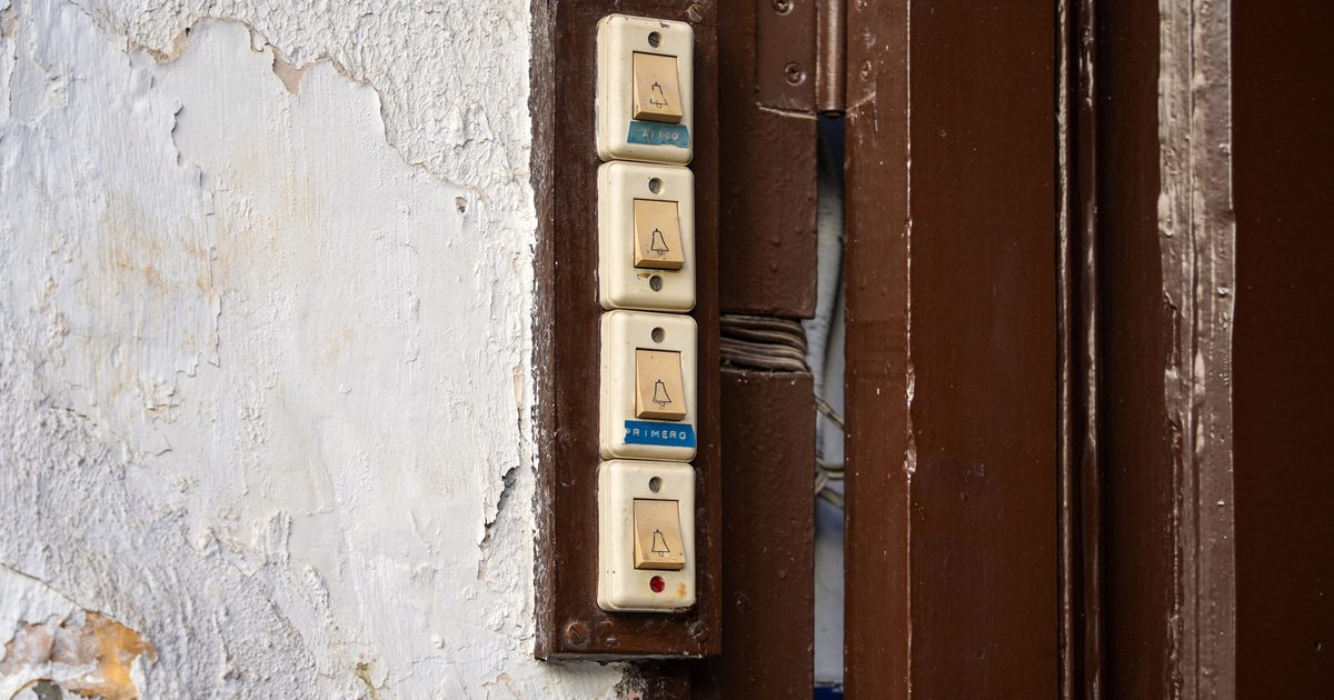 A column of four old cream-colored doorbell buttons, each marked with a small bell icon, mounted beside a brown wooden doorframe