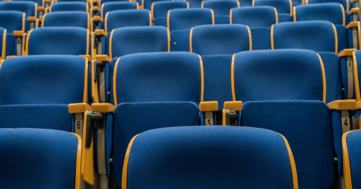 Rows of empty blue auditorium seats with wooden armrests and numbered seat plates
