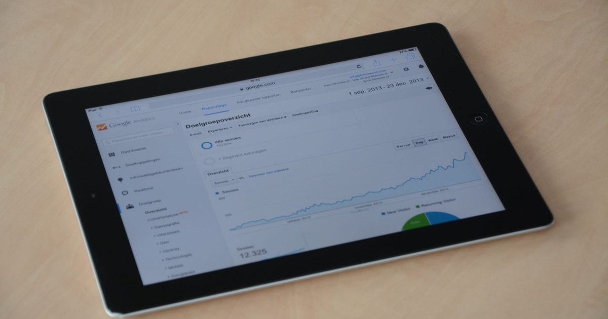 Tablet lying on a light wooden desk showing a web analytics overview with a rising traffic line chart