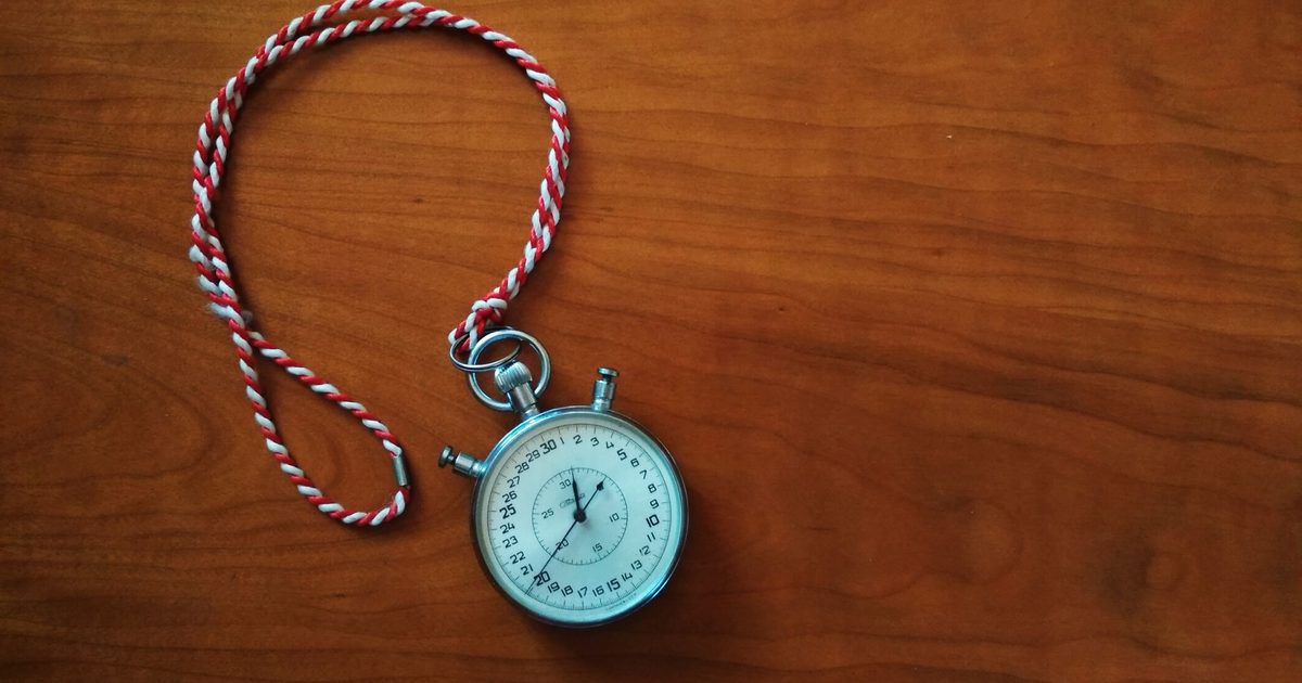 Silver analog stopwatch with a red and white cord lying on a brown wooden surface