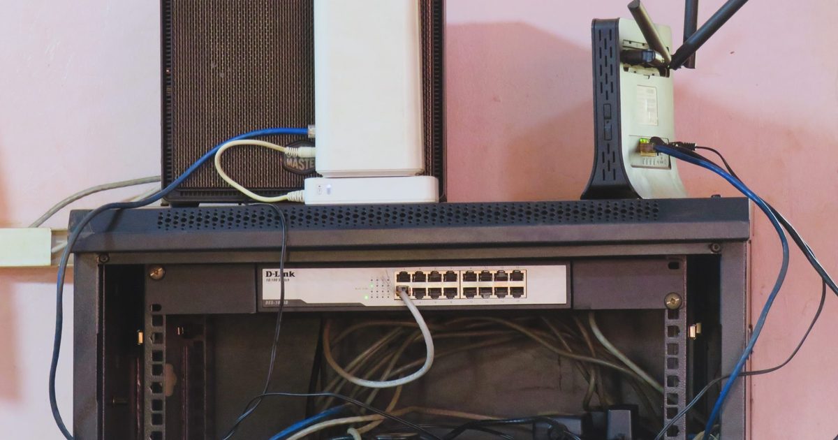 Wall-mounted network cabinet with a 16-port switch, a router and patch cables against a pink wall