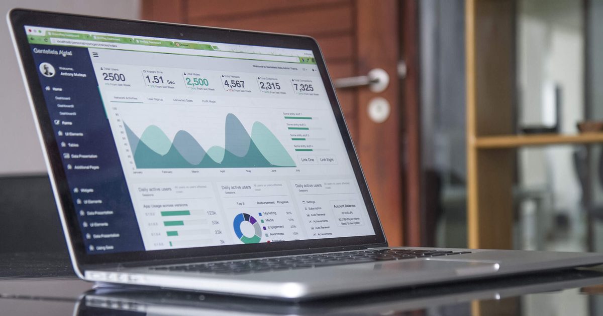 Laptop on a glossy desk showing an analytics dashboard with area charts, bar charts and headline numbers, reflected in the desk surface