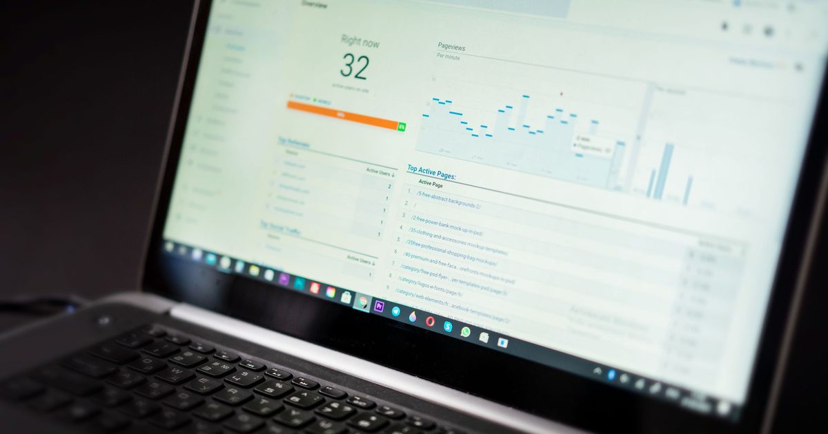 Laptop on a dark desk showing a Google Analytics real-time report with active users and a pageviews per minute chart