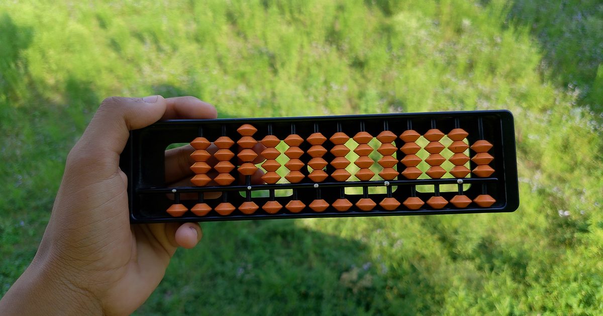 A hand holding a black abacus with rows of orange beads in front of a sunlit green lawn