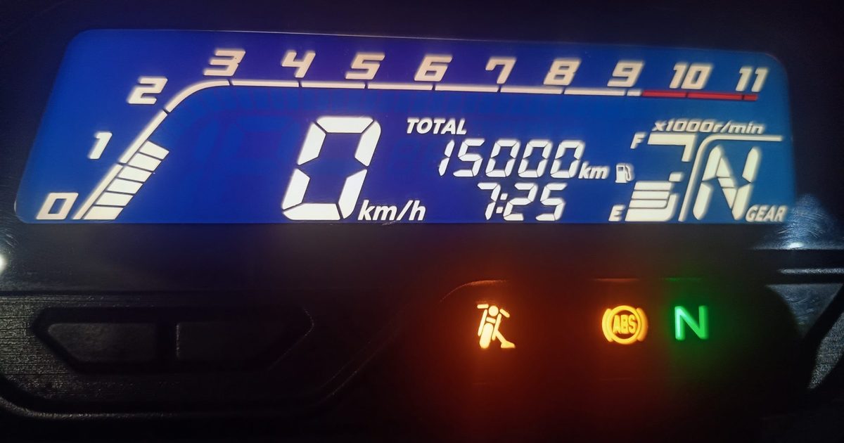 A motorcycle's blue digital dashboard at night showing a total of exactly 15,000 km on the odometer