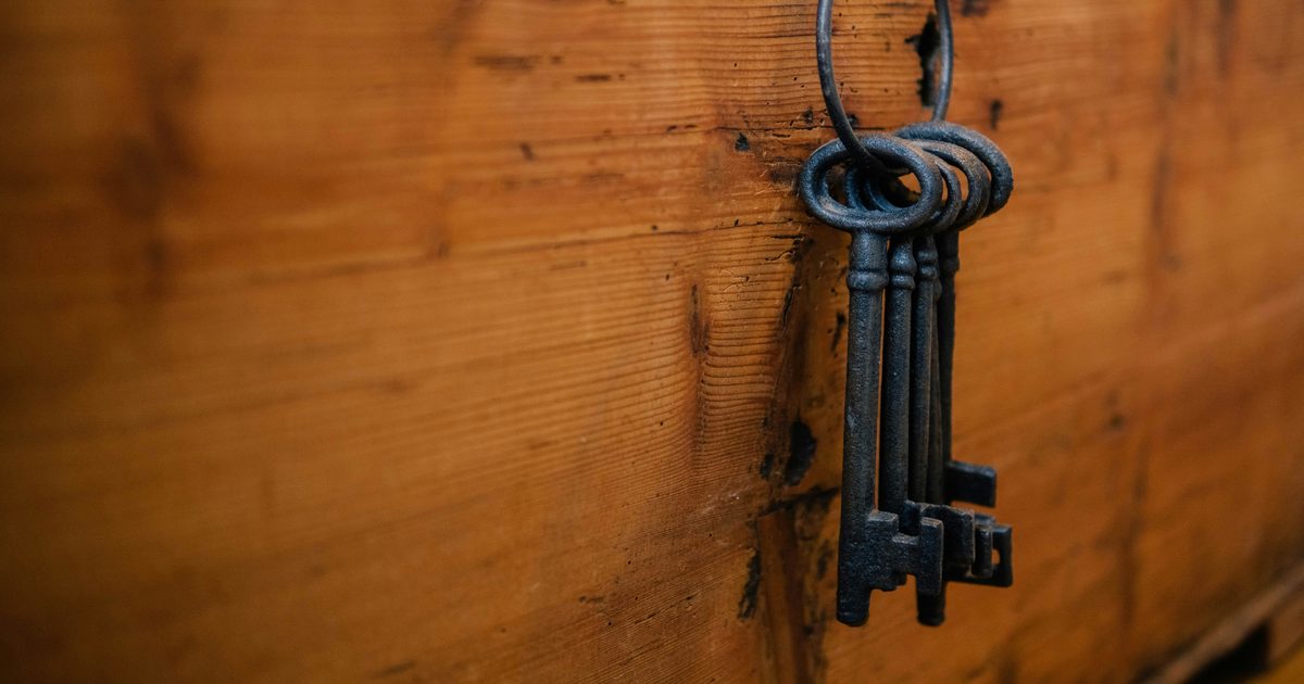 A ring of four old iron keys hanging from a nail on the side of a weathered wooden chest
