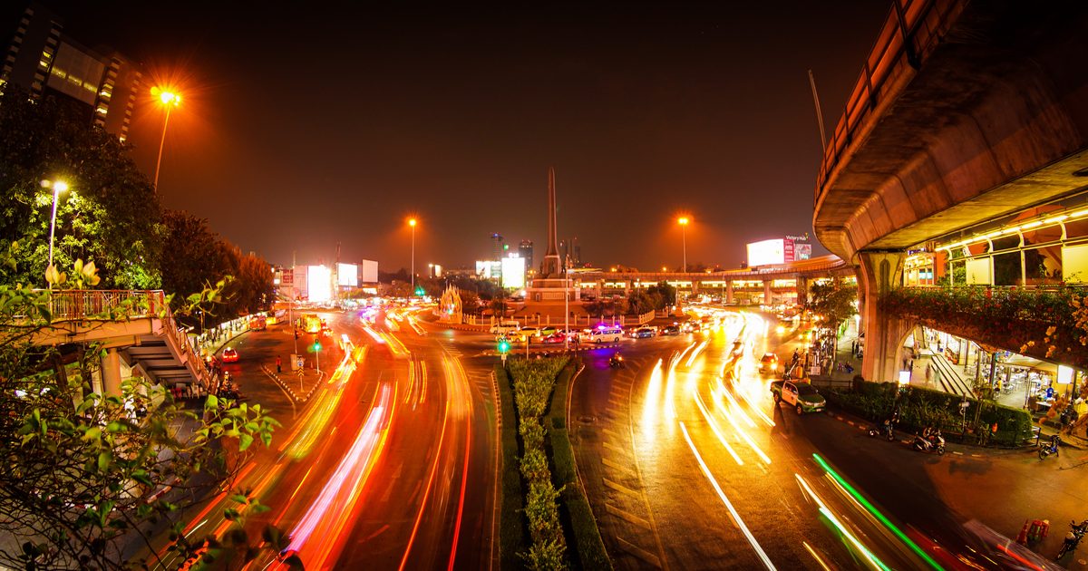 Long exposure photo of heavy night traffic in a city, with streaks of red and orange headlight trails merging at a busy intersection under an overpass