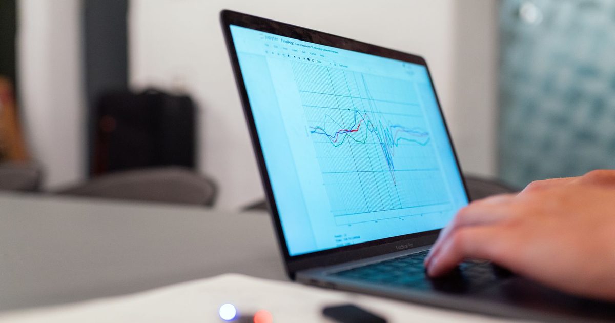 Hand typing on a laptop that shows a line chart with a sharp dip in the middle, in a softly lit living room