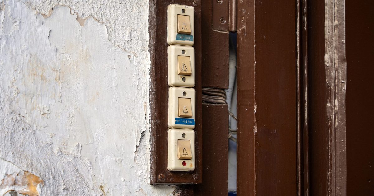 Four vintage doorbell buttons mounted in a column on a weathered wall beside a brown wooden door frame