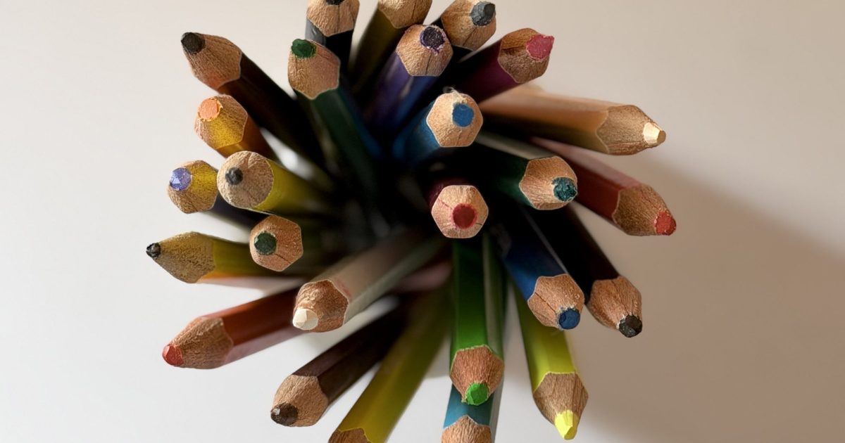 A top-down view of a bundle of sharpened colored pencils fanning out in a starburst on a white surface