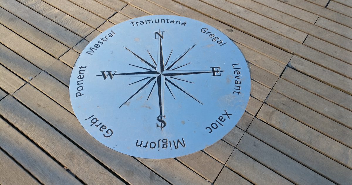 A round metal compass rose marked N, E, S and W set into a weathered wooden boardwalk